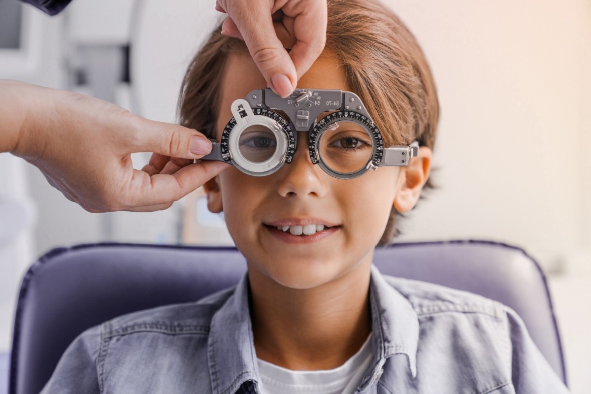 A young boy smiling while an optometrist adjusts a trial frame on his face during an eye exam.