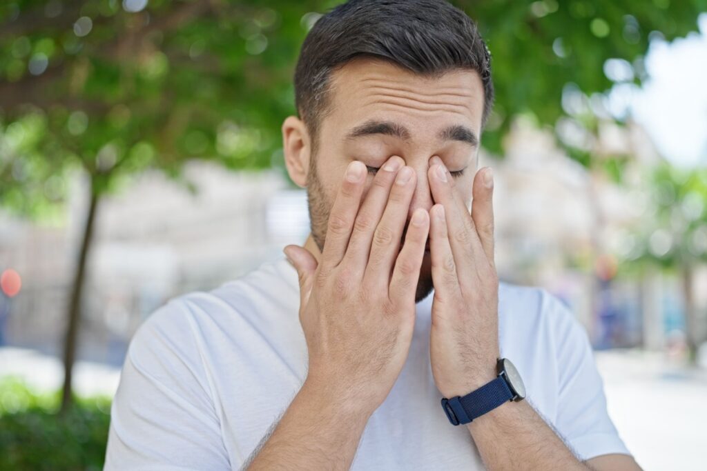 Man outside rubbing both eyes.